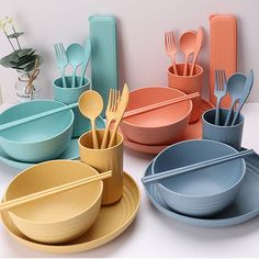 there are many different colored plates and bowls on the table with utensils in them