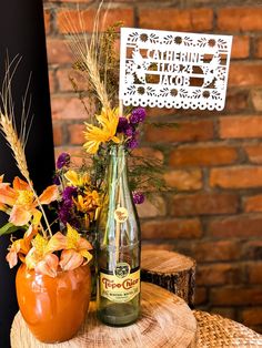 an orange vase filled with flowers sitting on top of a table next to a bottle