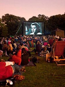 an outdoor movie theater with people sitting in lawn chairs and watching the movies on screen