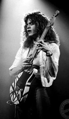 a man with long hair holding a guitar in front of a microphone on stage at a concert