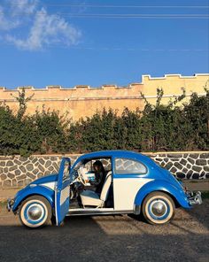 a blue and white car parked in front of a stone wall