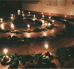 many candles are lit in the middle of a circle with greenery around it on a wooden floor