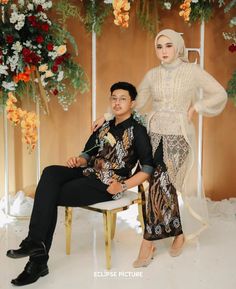 a man and woman sitting next to each other in front of a backdrop with flowers