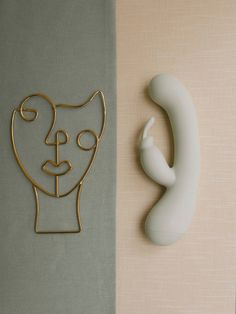 a white vase sitting next to a wall with a gold cat head on it's side