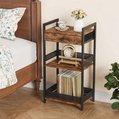 a small wooden shelf with books on it next to a bed and potted plant