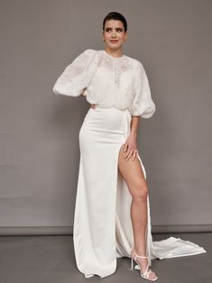 a woman posing in a white gown with her legs crossed and wearing high heeled sandals