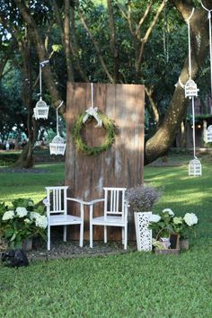 two white chairs sitting in front of a wooden structure with wreaths hanging from it