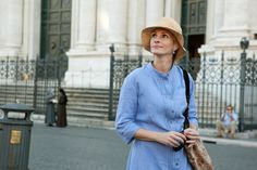 a woman in a blue shirt and hat is standing on the street with her hands behind her back