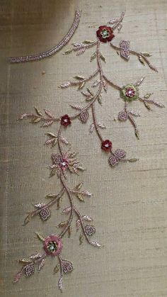 an embroidered piece with flowers and leaves on it's side, sitting on a table