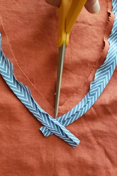 someone is cutting fabric with scissors on a piece of blue and orange material that has been taped to it