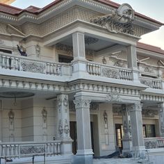 a man standing on the balcony of a large white building with ornate carvings and columns