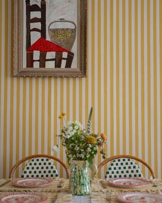 a vase with flowers sitting on top of a table next to two chairs and a painting