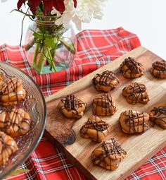 some cookies are sitting on a wooden board next to a glass vase with flowers in it