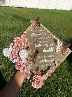 someone is holding up a graduation cap decorated with flowers and butterflies on the grass in front of them