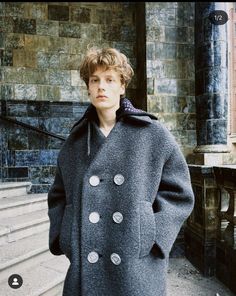 a man standing in front of some steps wearing a gray coat and black pants with buttons on it