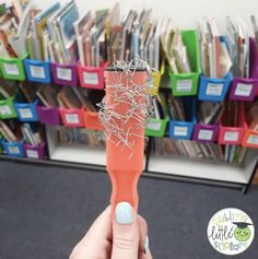 a hand holding an orange toothbrush in front of a pile of books