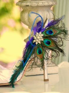 a peacock feather shoe decoration sitting on top of a white table next to a vase