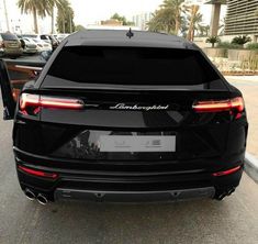 the back end of a black suv parked in a parking lot next to palm trees