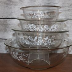 four glass bowls are stacked on top of each other in front of a wooden table