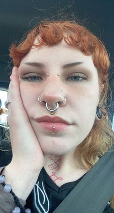 a woman with red hair and piercings on her nose is sitting in a car