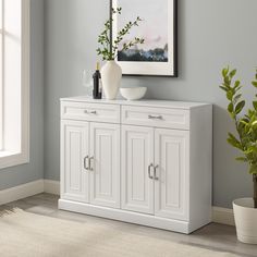 a white cabinet with two doors and drawers in a room next to a potted plant