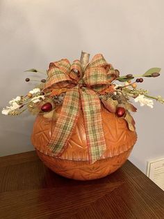 an orange pumpkin with a bow on top of it sitting on a table next to a wall