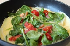 a pan filled with spinach, tomatoes and cheese