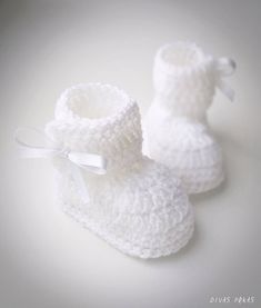 a pair of white crocheted baby booties with a bow on the side