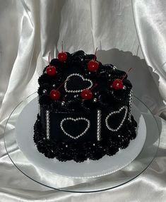 a black cake with hearts and cherries on it sitting on a glass platter