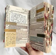 an open book with writing on it in someone's hand and papers taped to the pages