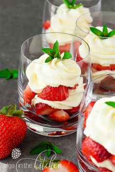 four desserts with strawberries and whipped cream on top are arranged in glass bowls