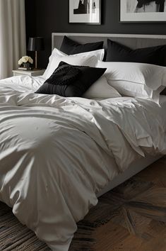 a bed with white sheets and black pillows in a dark room next to a window