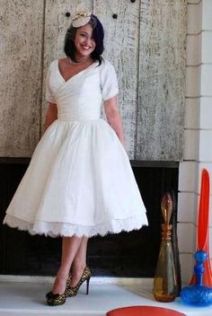 a woman standing in front of a fireplace wearing a white dress and high heel shoes