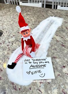 an elf sitting on top of a table next to a sign