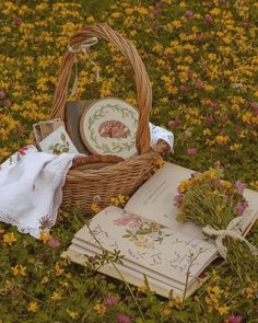 a wicker basket filled with flowers next to an open book on top of a field