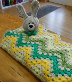 a crocheted blanket with a stuffed animal on it sitting on a wooden table