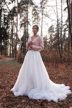 a woman is standing in the leaves wearing a wedding dress and holding her hands together