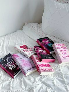 a pile of books sitting on top of a bed next to pillows and pillow cases