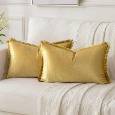 two yellow pillows sitting on top of a white couch next to a vase with flowers