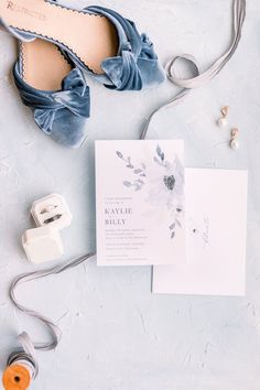 wedding stationery and accessories laid out on top of a blue surface with white flowers