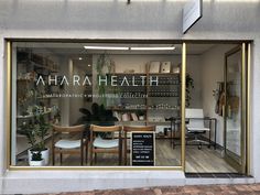 the front window of a store with wooden chairs and plants in it's windows