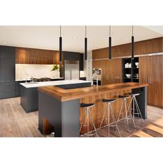 a large kitchen with wooden floors and black cabinets, bar stools, and an island in the middle