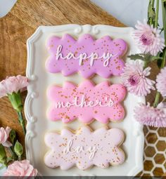 three decorated cookies sitting on top of a white plate next to pink and purple flowers