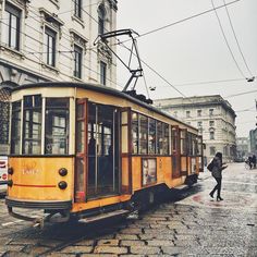 an old yellow trolley car is parked on the cobblestone street in front of some buildings