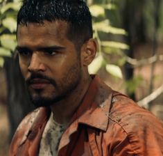 a close up of a person wearing a leather jacket in the woods with trees behind him