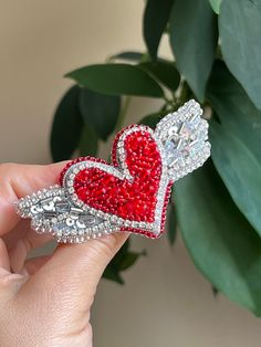 a person holding a red heart shaped brooch with wings on it's side