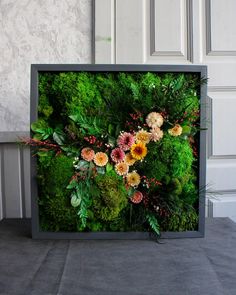 an arrangement of flowers and greenery in a black frame