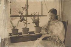 an old black and white photo of a woman sitting at a desk with potted plants