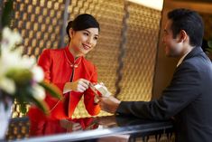 a man handing something to a woman in a red dress sitting at a table with flowers on it