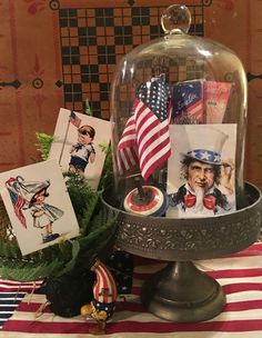 a glass cloche with pictures and flags under it on a table next to a potted plant